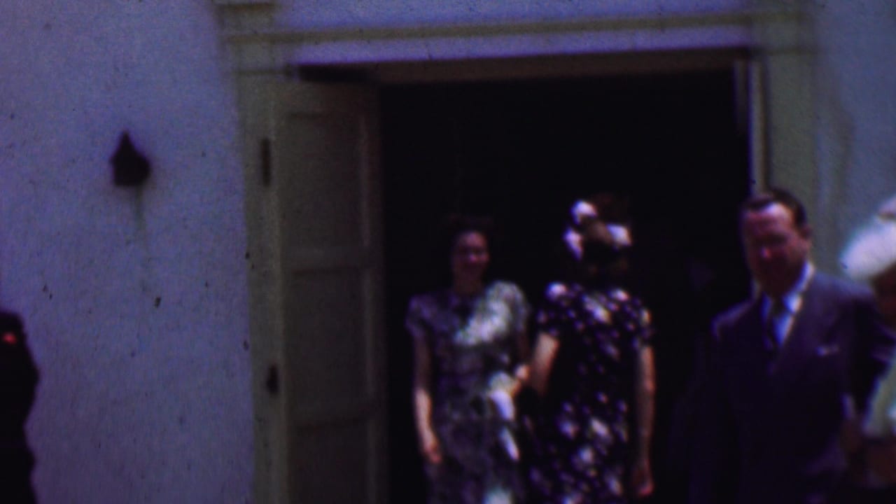In supported 1956 Dallas home-movie footage, three formally dressed adults walk out from a church entrance, with hats, patterned dresses, and a suit visible in soft 8mm color.