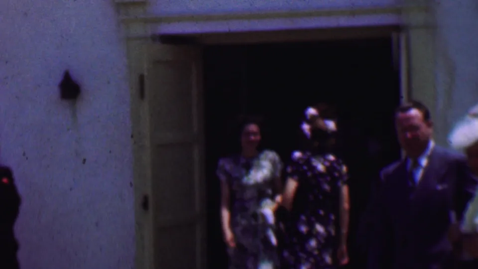 In supported 1956 Dallas home-movie footage, three formally dressed adults walk out from a church entrance, with hats, patterned dresses, and a suit visible in soft 8mm color.