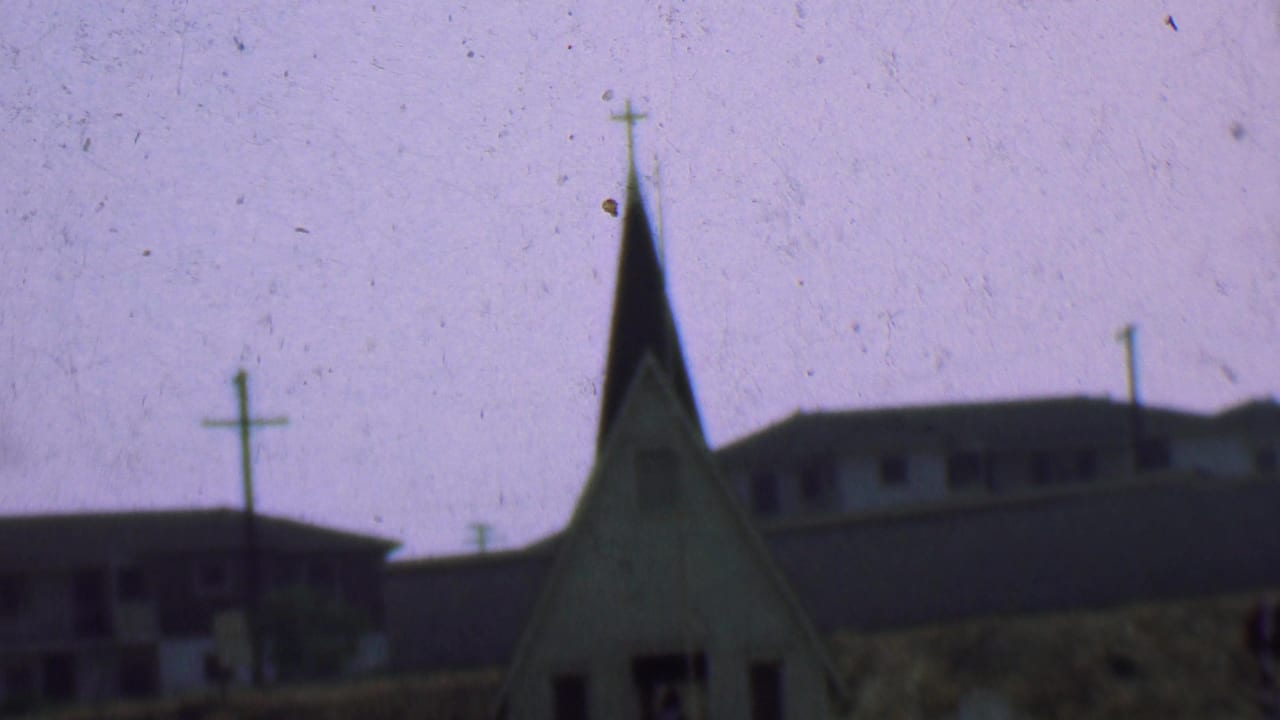 Church steeple with cross stands beside low buildings and utility poles.