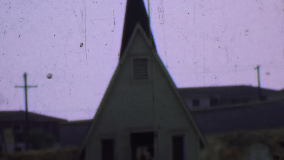 The final frame holds on the church facade in the supported 1956 Dallas setting, with the steeple, cross, doorway, side windows, background buildings, and small marker-like objects visible.