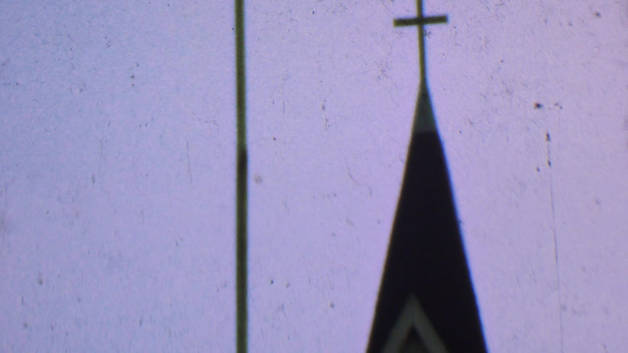 Dallas, Texas 1956 8mm frame showing the upper point of a church steeple with a small cross and a tall pole against a pale gray sky.