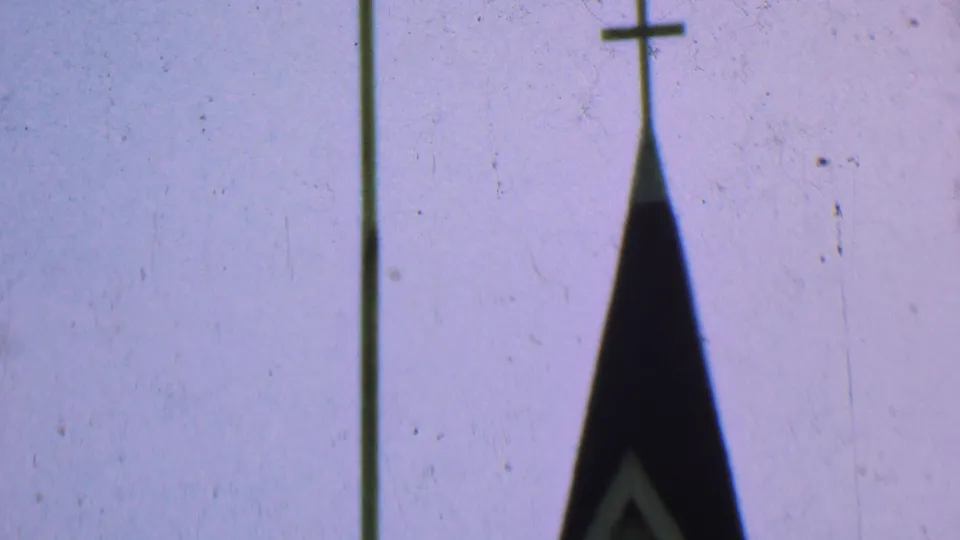 Dallas, Texas 1956 8mm frame showing the upper point of a church steeple with a small cross and a tall pole against a pale gray sky.