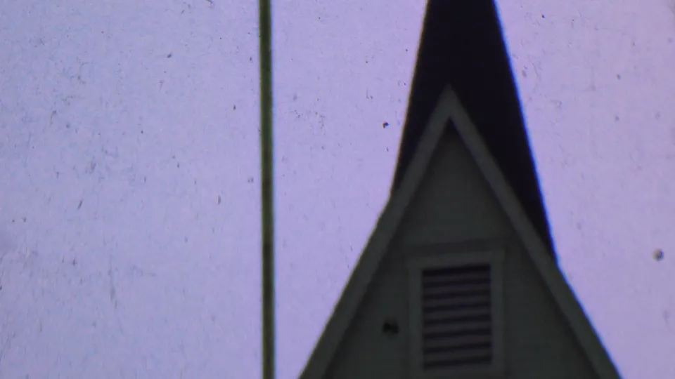 Dallas, Texas 1956 8mm frame showing more of the church steeple, including pale trim, horizontal siding, a louvered vent, and a pole to the left.