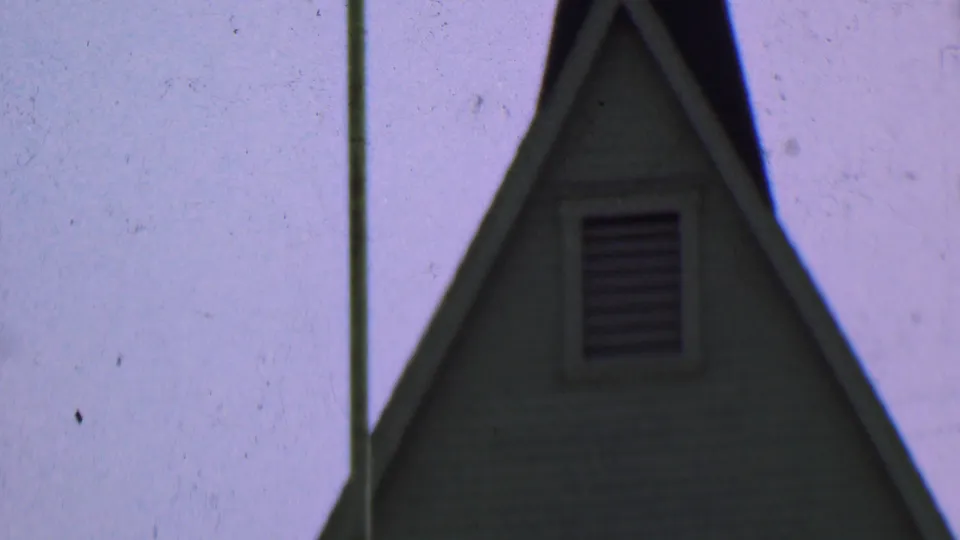 Dallas, Texas 1956 8mm frame of the church's steep dark roof, white-trimmed gable, louvered vent, horizontal siding, and adjacent tall pole.