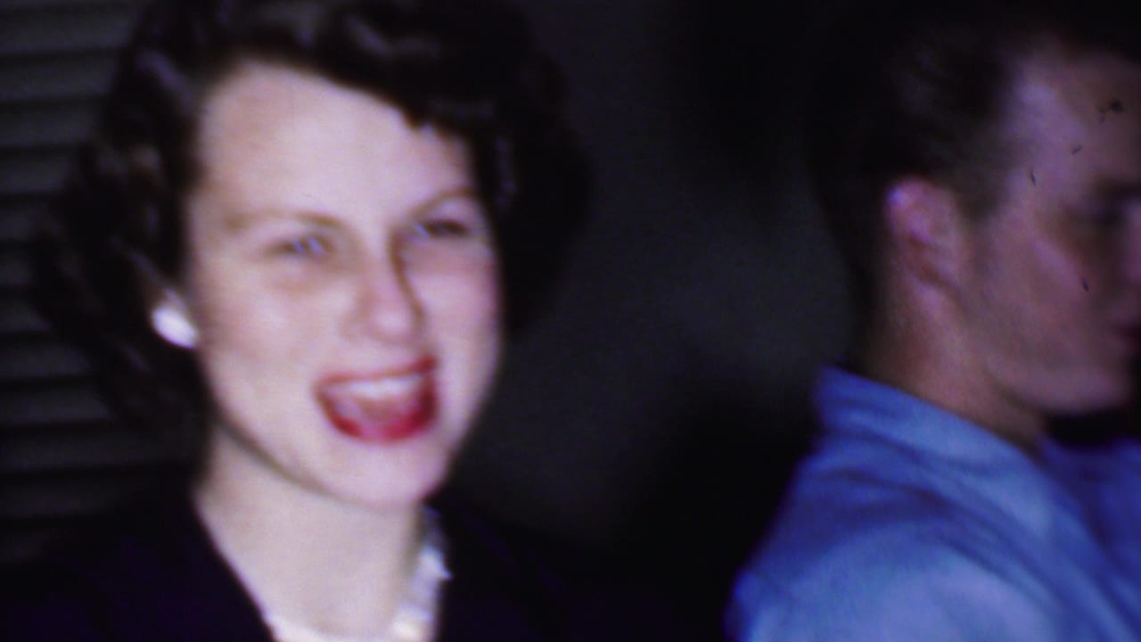 Smiling woman in dark clothing and pearls beside a man in a light blue shirt.