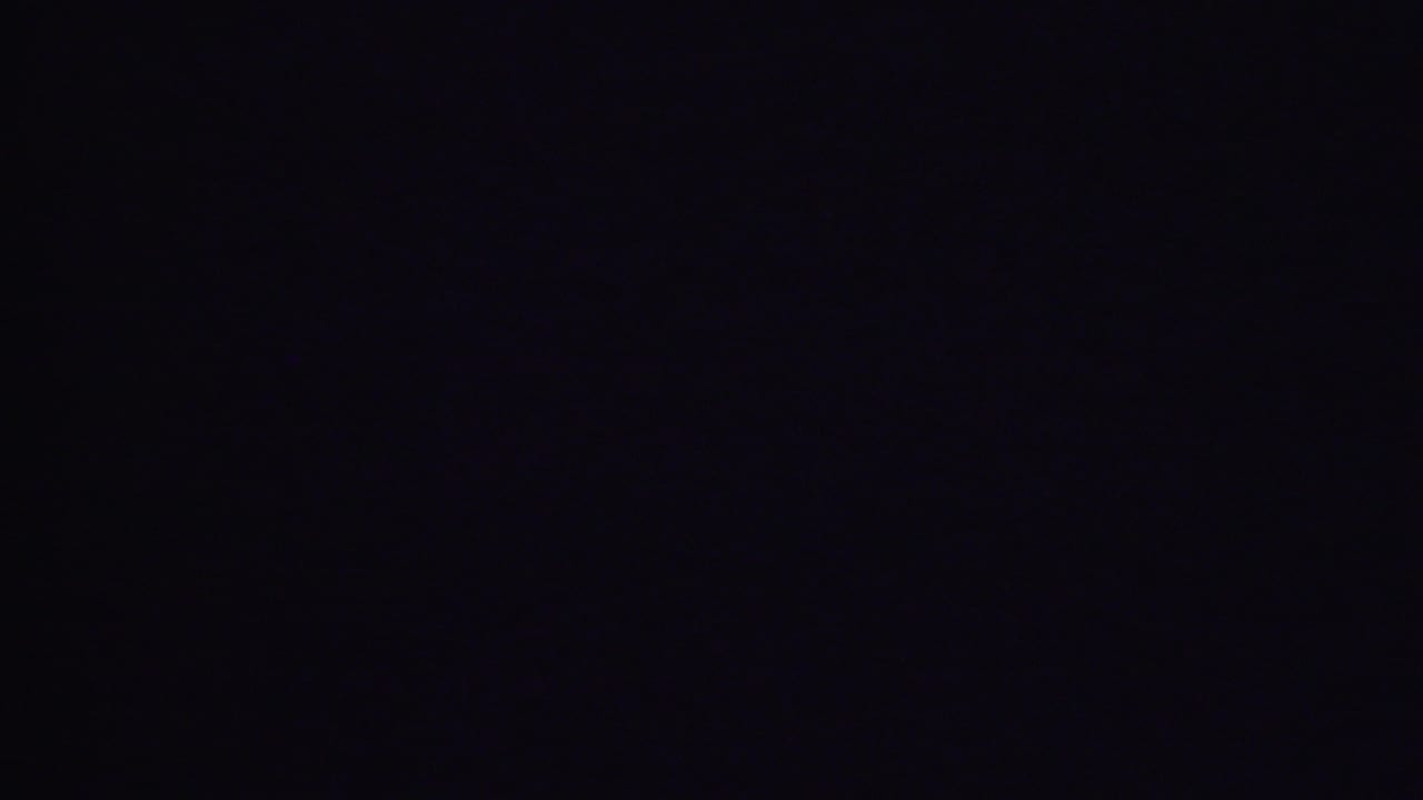 Underexposed 1956 Phoenix home-movie frame from a domestic interior, with most visible detail lost to darkness and faint film specks present.