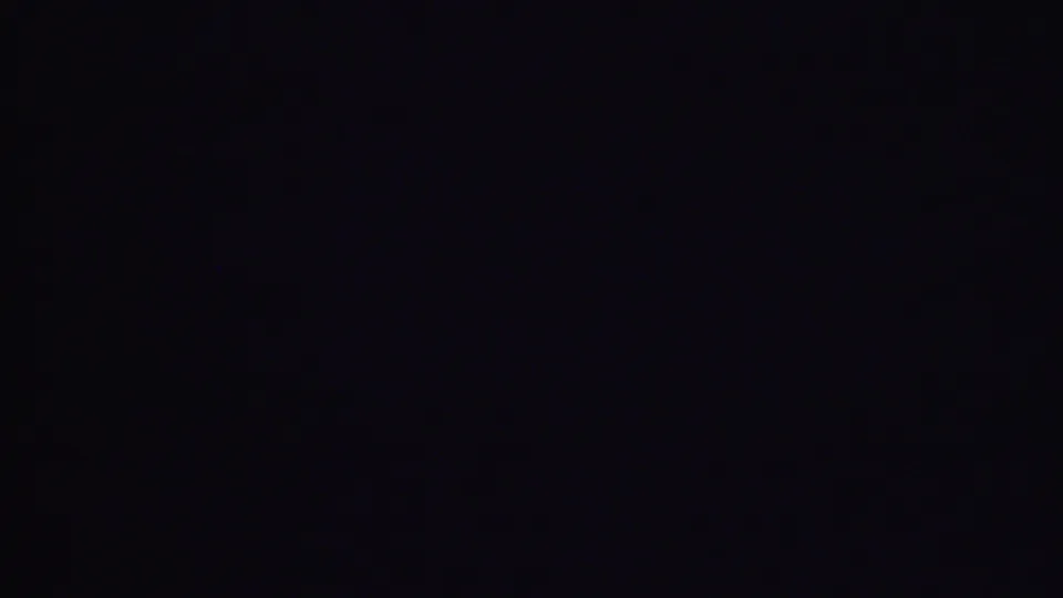 Underexposed 1956 Phoenix home-movie frame from a domestic interior, with most visible detail lost to darkness and faint film specks present.