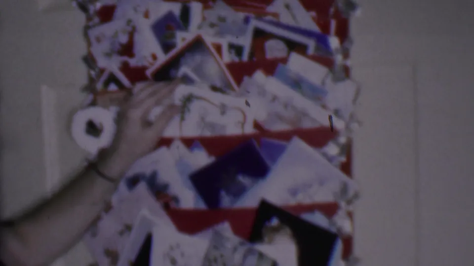 Phoenix, Arizona 1956 home-movie frame showing a hand placing or adjusting a holiday card on a red wall shelf beneath a lit red candle.