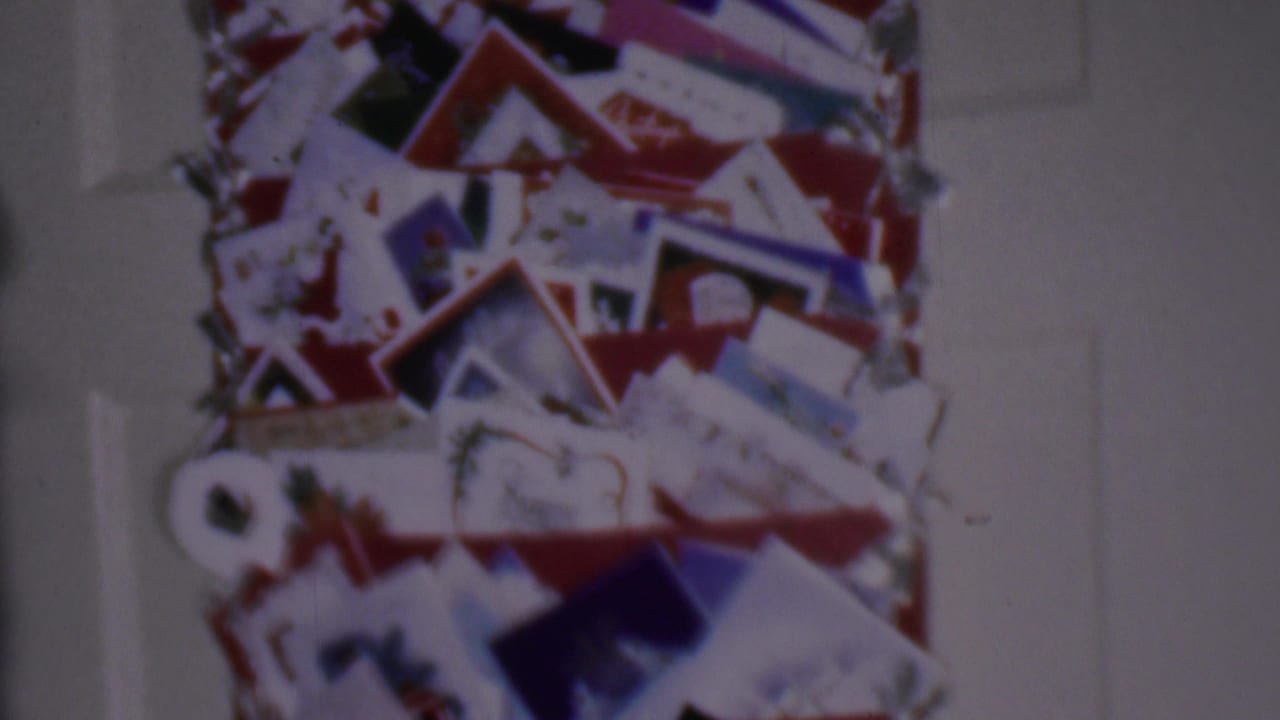 1956 Phoenix home-movie frame showing a close view of Christmas cards and letters gathered on a red-accented display inside a private home.