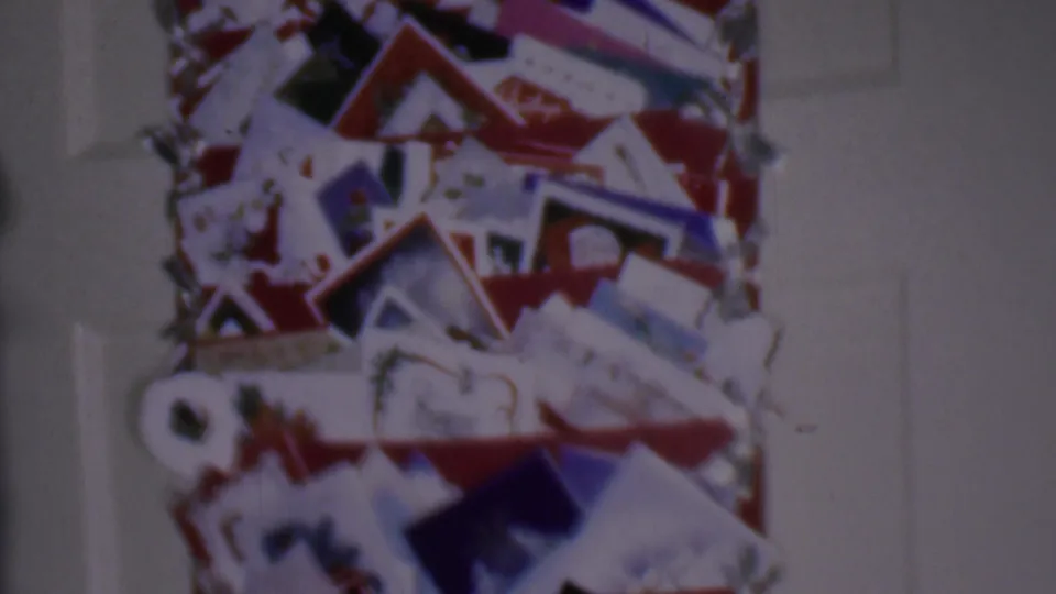 1956 Phoenix home-movie frame showing a close view of Christmas cards and letters gathered on a red-accented display inside a private home.