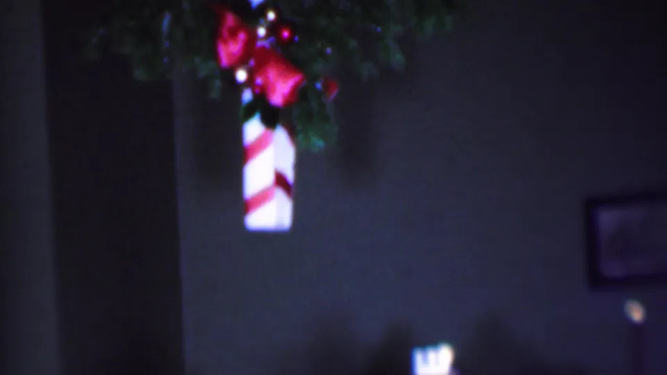 Soft 8mm frame from the Phoenix holiday footage showing the candy cane decoration partly at the edge of the frame with greenery, ribbon, wall space, and interior room details.