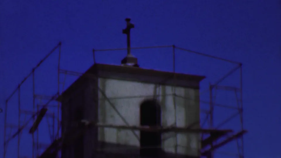 Later frame of the 1956 Dallas church construction scene, with the scaffolded tower, arched opening, and rooftop cross centered against the twilight sky.