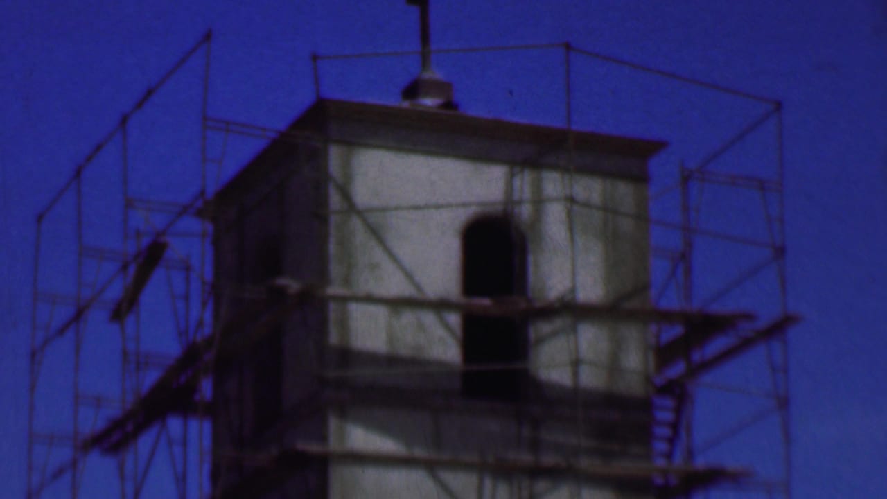 1956 Dallas 8mm frame showing a concrete tower with metal scaffolding, arched openings, and a deep blue sky.