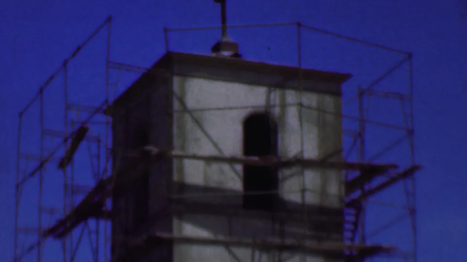 1956 Dallas 8mm frame showing a concrete tower with metal scaffolding, arched openings, and a deep blue sky.