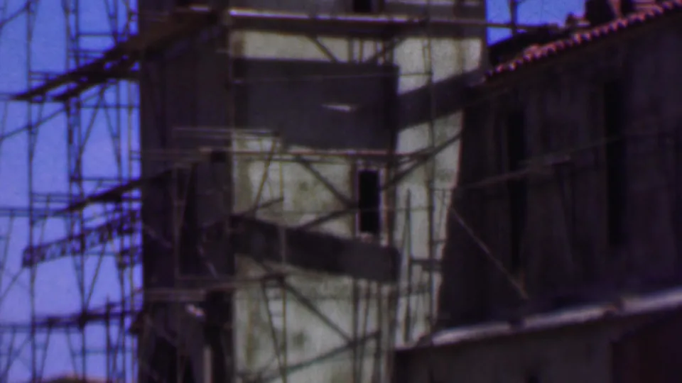 1956 Dallas 8mm frame showing a scaffolded building facade with a pale tower-like section, dark openings, and adjacent roofline under blue sky.