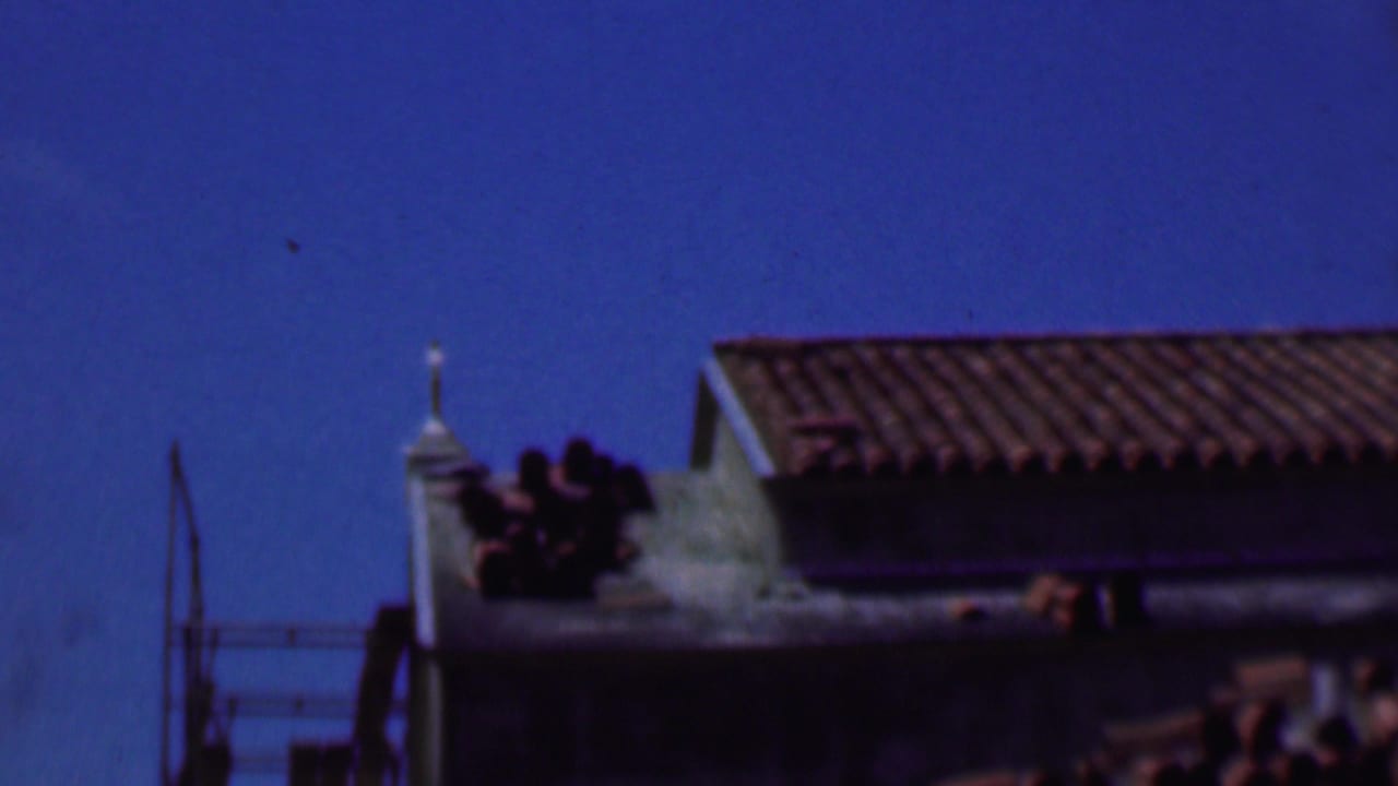 Two rooflines with tile roofs and a small white finial against blue sky.
