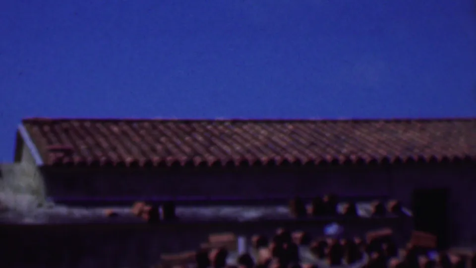 1956 Dallas 8mm frame of a long terracotta-tiled roof with dark eaves, pale stucco edges, and a saturated blue sky.