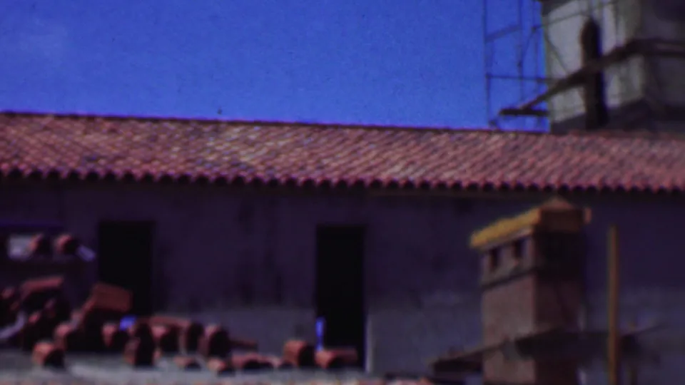 1956 Dallas 8mm frame with the camera panning along a red tile roof, dark wall openings, and construction or restoration materials below.