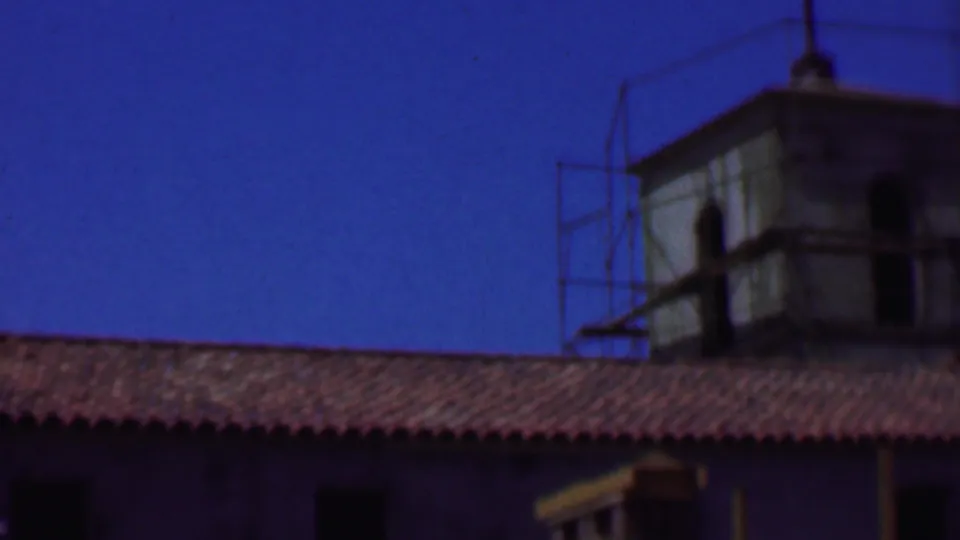 1956 Dallas frame showing a red tile roof in the foreground and a tower-like structure with scaffolding against a clear blue sky.
