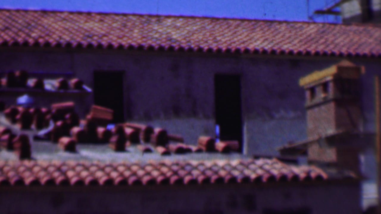 Stacks of red roof tiles on a sloped roof beside unfinished wall openings.