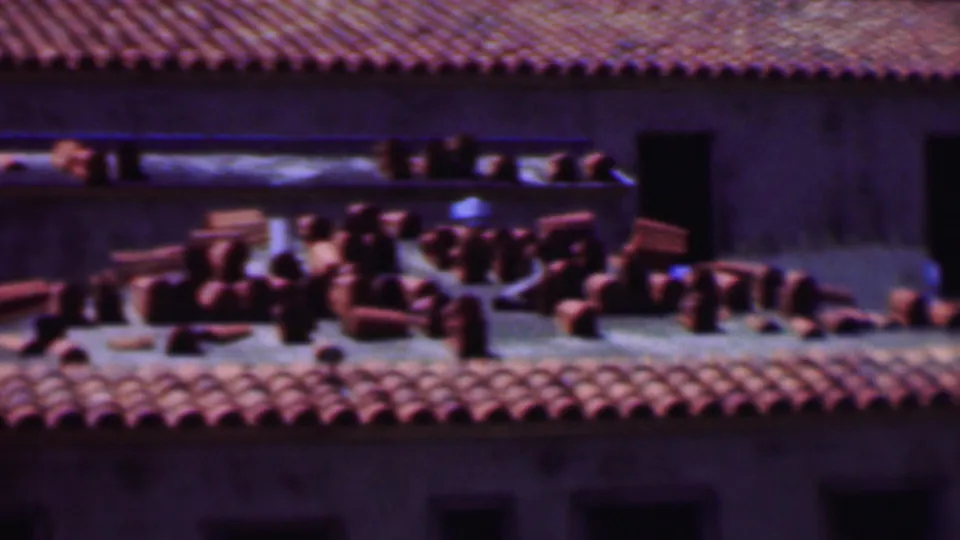 1956 Dallas 8mm frame showing red roofing tiles arranged on a rooftop work area below a masonry wall with dark rectangular openings.