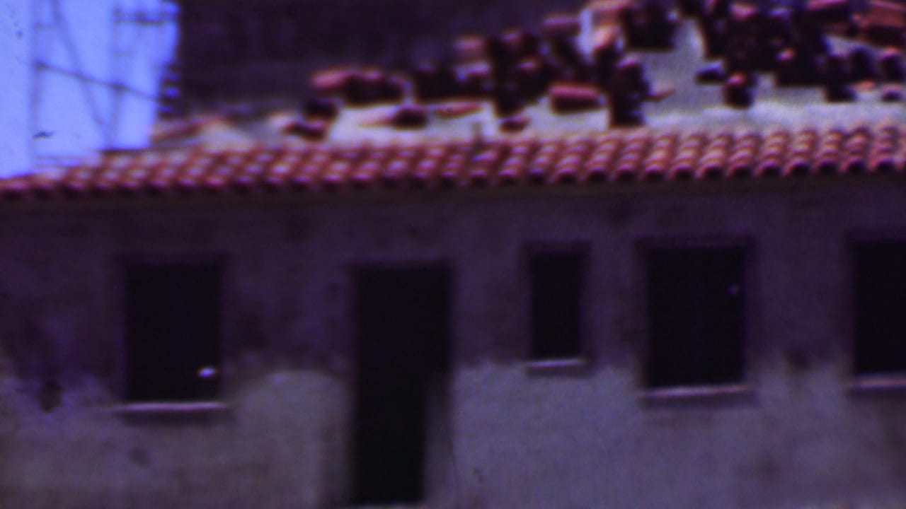 1956 Dallas 8mm frame showing a weathered building exterior with a red tile roof, dark windows, and rooftop materials in soft, color-shifted film.