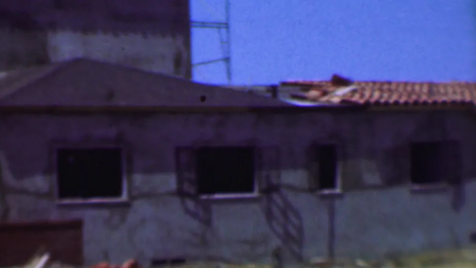 Dallas, Texas construction frame from the supplied 1956 footage showing an unfinished wall with several dark window openings, a low roofline, and red tile roofing visible at the upper right.