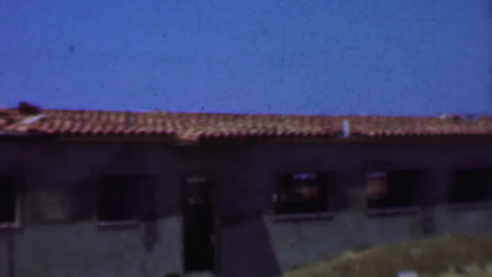 1956 Dallas frame of a low-slung building under renovation, with terracotta roof tiles, unfinished concrete walls, dark window openings, and open doorways.