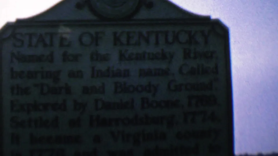 1961 Covington, Kentucky 8mm frame showing the upper portion of a dark green State of Kentucky historical marker with softened inscription text.