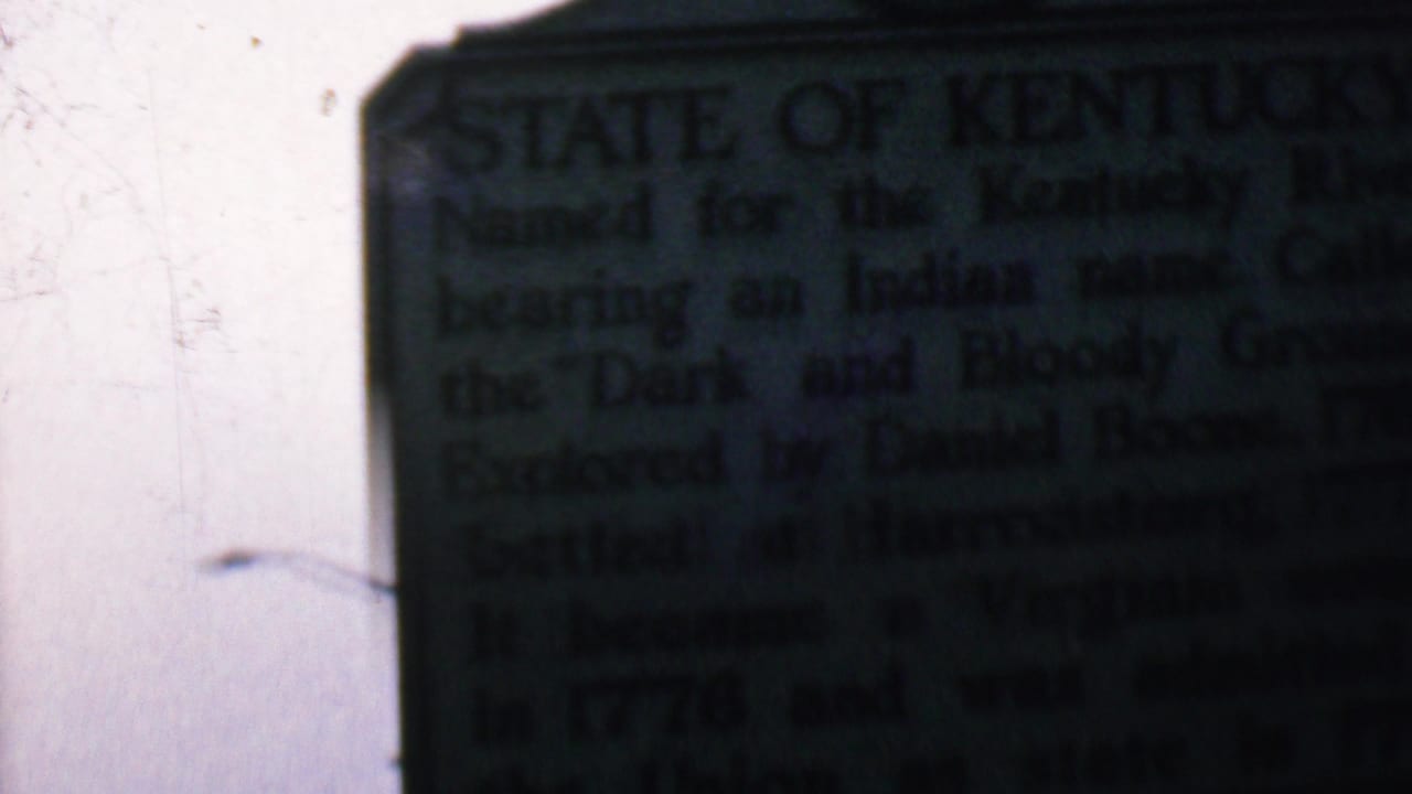Dark Kentucky historical marker fills the right side of the frame with pale sky at left.