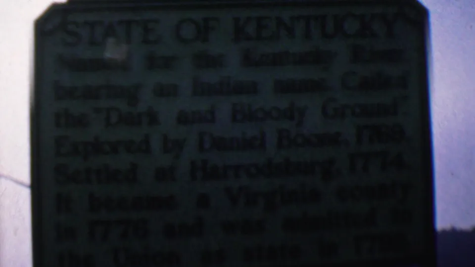 Close 1961 home-movie view of the Kentucky state history plaque, with lines about the Kentucky River, Daniel Boone, and Harrodsburg partially readable.