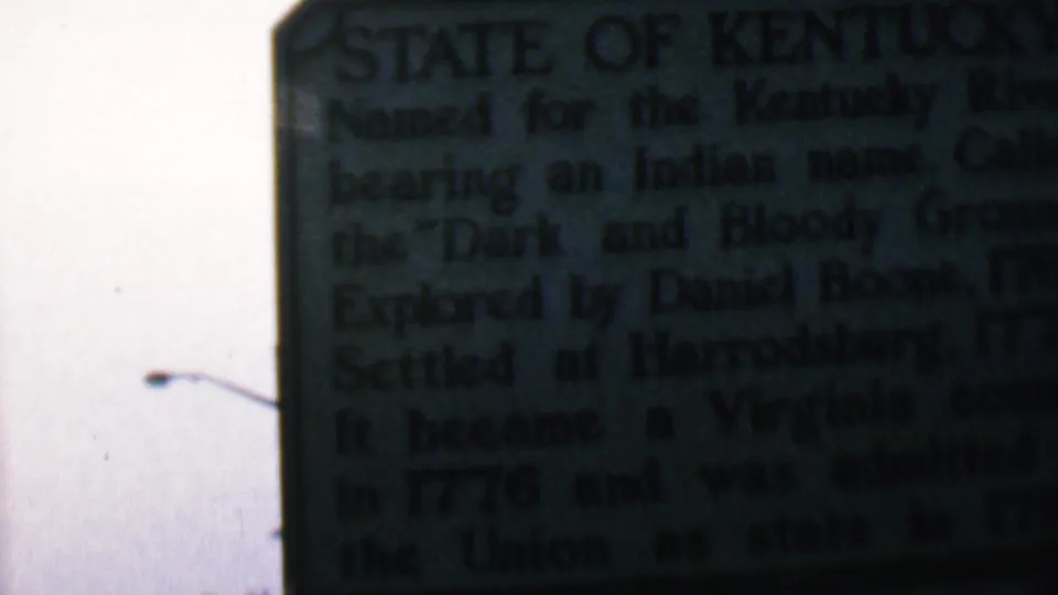 Final 8mm frame of the Covington Kentucky marker, showing the plaque text in dark exposure with a streetlight silhouette and pale sky to the left.