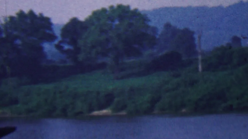 End frame of the 8mm river view showing broad water, wooded banks, a small barge edge in the foreground, and hazy hills beyond.