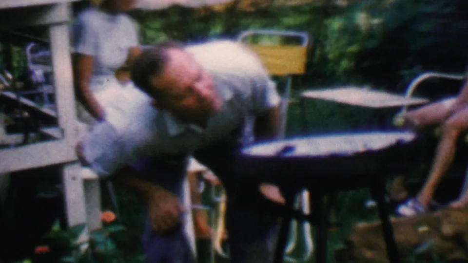 The man bends beside the round grill while a woman in a white dress and another cropped seated adult remain nearby in the 1961 Covington backyard scene.