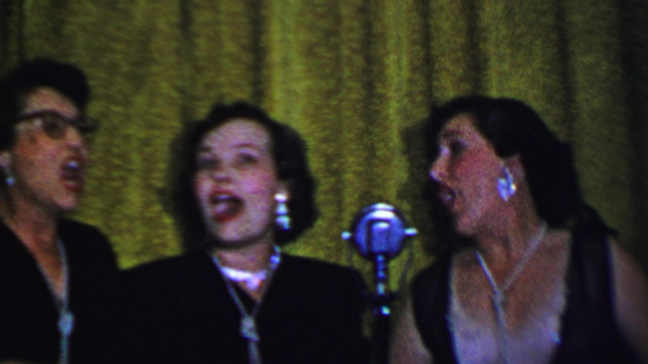 Three adult women in formal dark clothing sing near classic silver microphones, with jewelry and a textured green curtain visible in the 1956 Dallas footage.