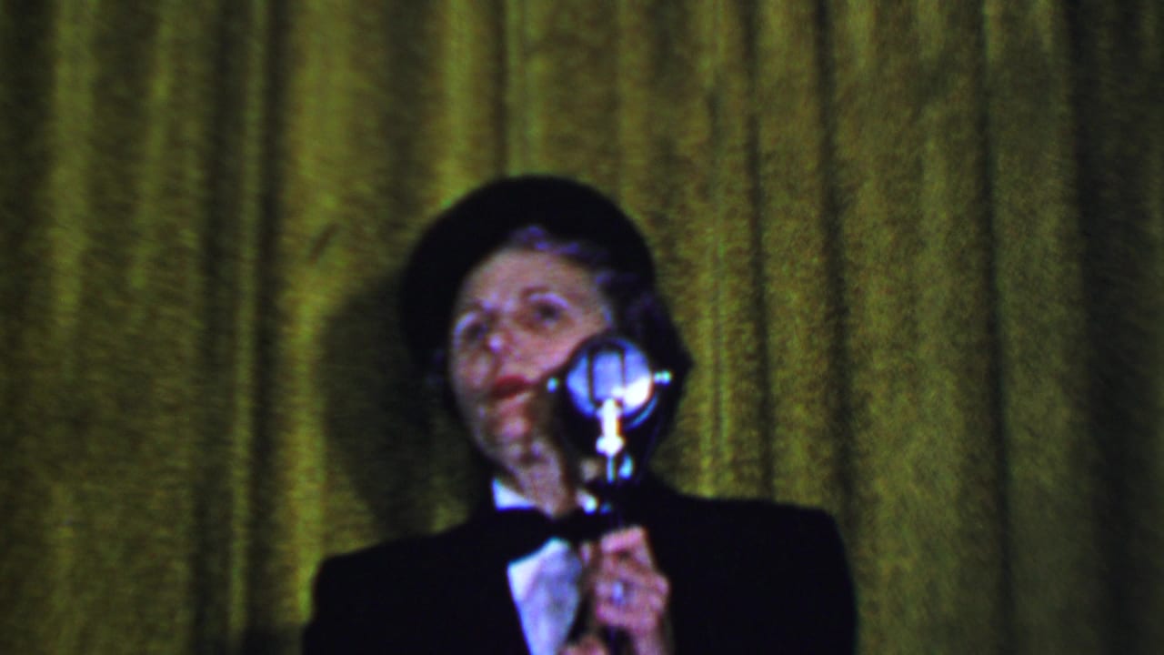 Woman stands at a silver microphone with her face turned slightly upward against a green curtain.