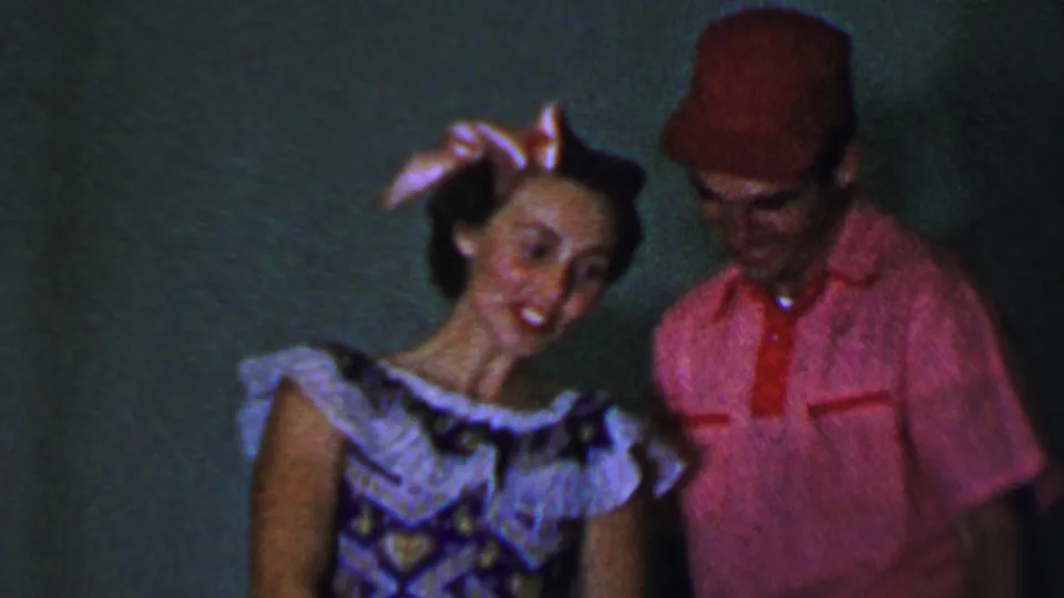 The duet partners stand close together in the Dallas 1956 home-movie frame, with the woman smiling and leaning toward the man as he looks downward.