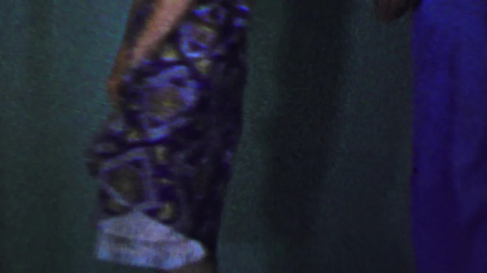 Near the end of the 1956 Dallas clip, the woman moves across the frame in her patterned dress while the man is partly cropped and a blue curtain or wall edge appears at right.