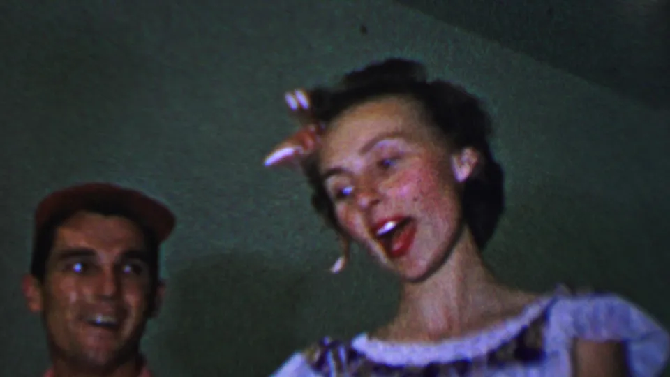 The young woman appears to sing or call out while the young man in a red cap looks toward her in this colorful 1956 Dallas 8mm home-movie frame.