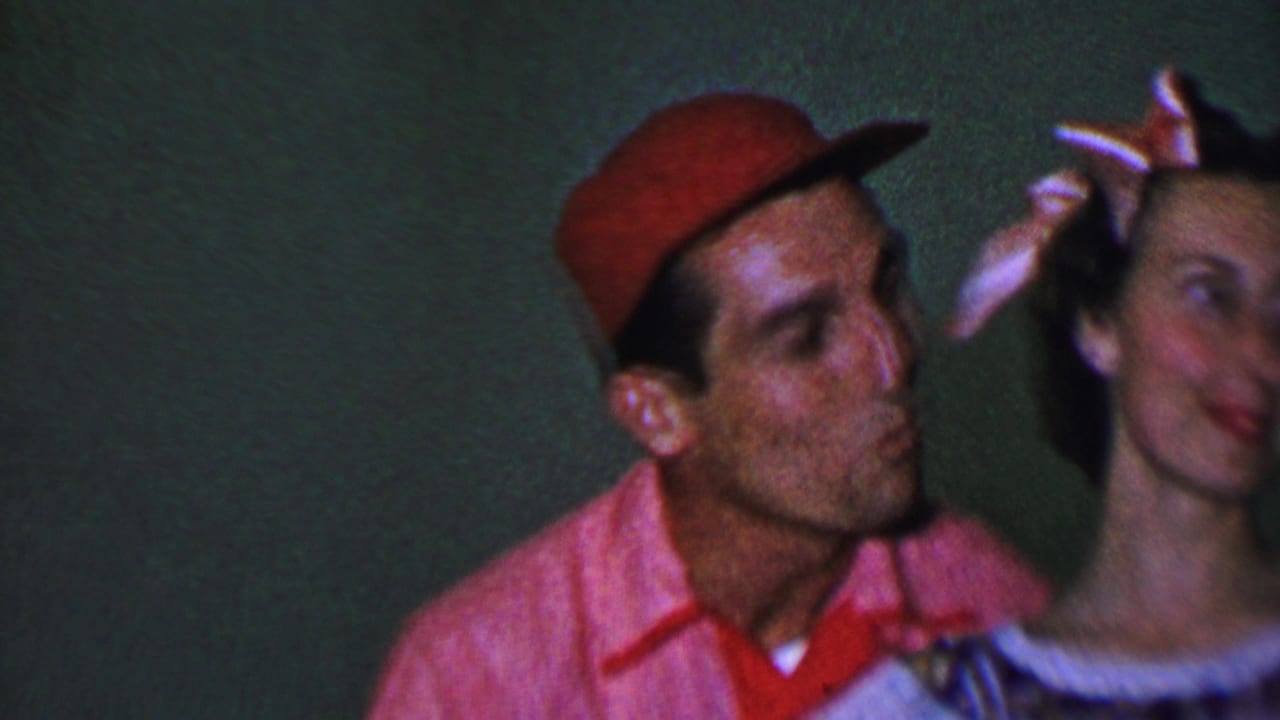 Man in a red cap leans toward a woman with a bow in her hair.