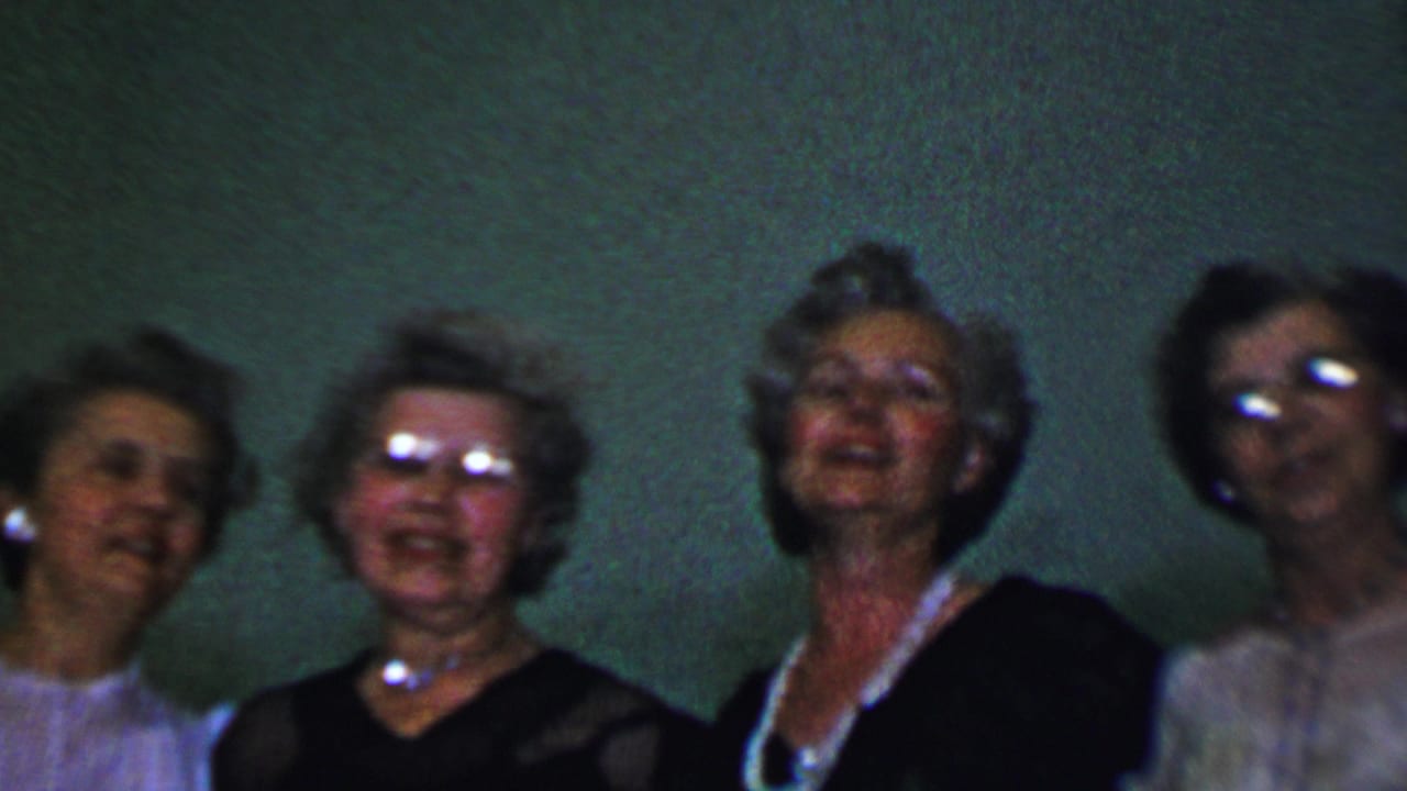Dallas, Texas 1956 home-movie frame showing several adult women singing in a small choral group, with styled hair, dresses, jewelry, and eyeglasses visible.