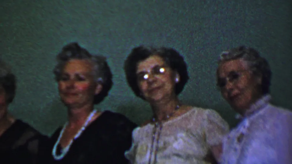 A closer handheld view shows adult women in formal clothing and pearl jewelry, with one figure partly cut off at the left edge.