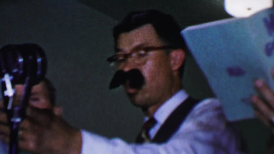 In the final frame, the man with glasses and a fake mustache sings beside a standing microphone while another songbook remains close to the camera.