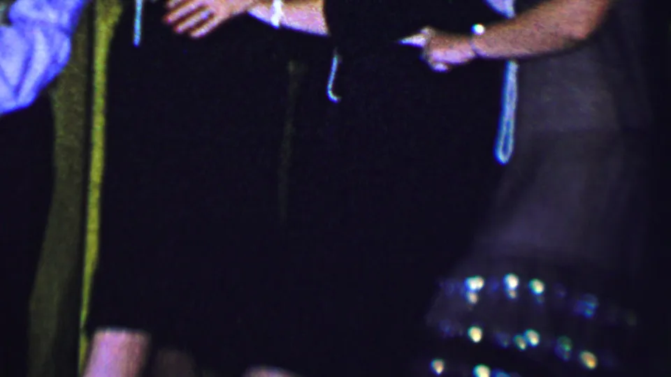 A close, soft-focused 1956 Dallas home-movie frame shows formally dressed women standing together with pearls and earrings before a gold curtain.