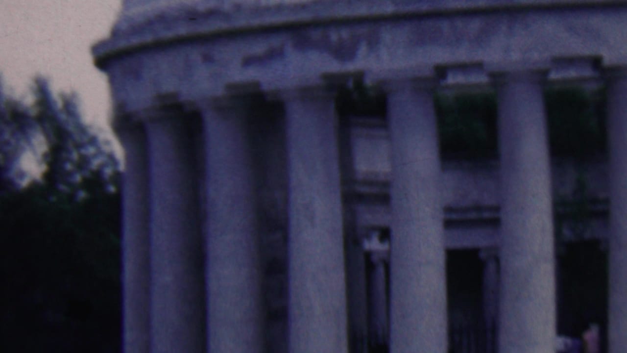 1961 Covington, Kentucky home-movie frame showing a neoclassical stone structure with fluted columns, shadowed openings, and trees along the left edge.