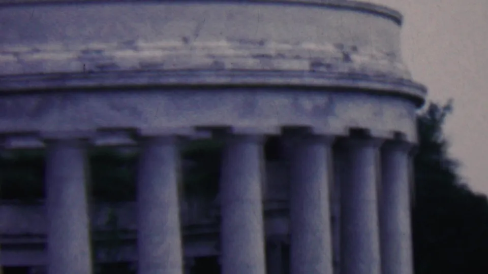 1961 Covington, Kentucky home-movie still showing the upper portion of a rounded colonnade, with stone columns, dark openings, and trees in the background.