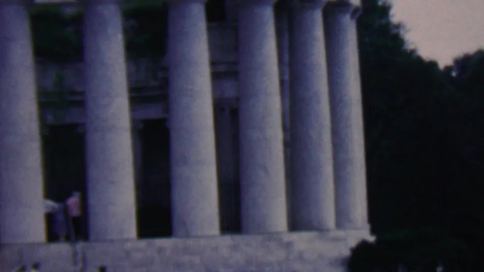 1961 Covington, Kentucky frame showing tall stone columns, a shadowed central opening, surrounding trees, and an indistinct visitor near the base of the structure.