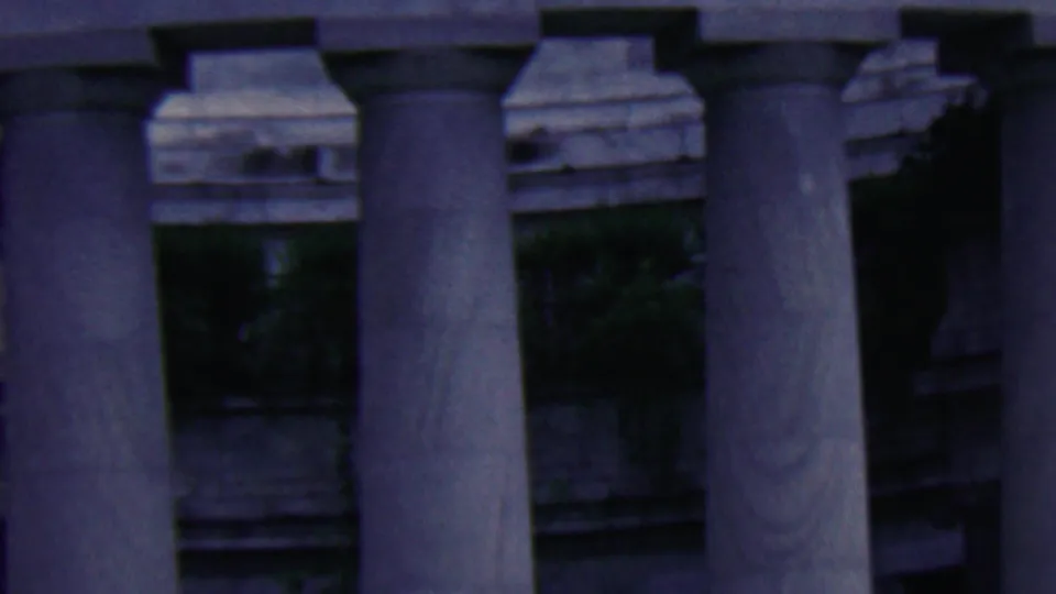 Soft 8mm frame showing massive stone columns, carved trim, shadowed openings, and greenery at the Covington monument.