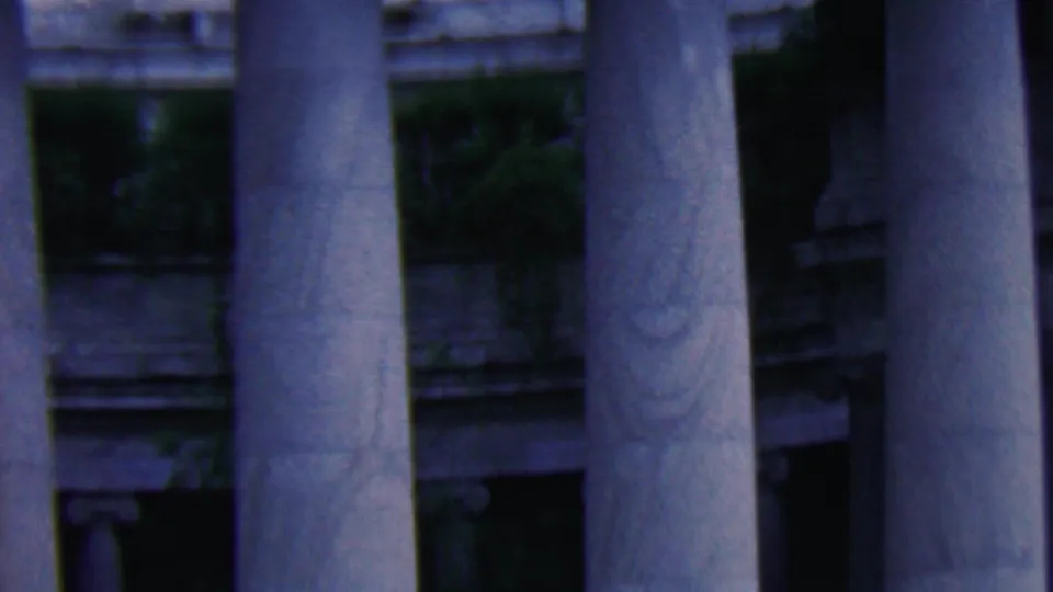 Final frame of the 1961 Covington home movie clip, dominated by tall stone columns with shadowed portico areas and greenery behind them.