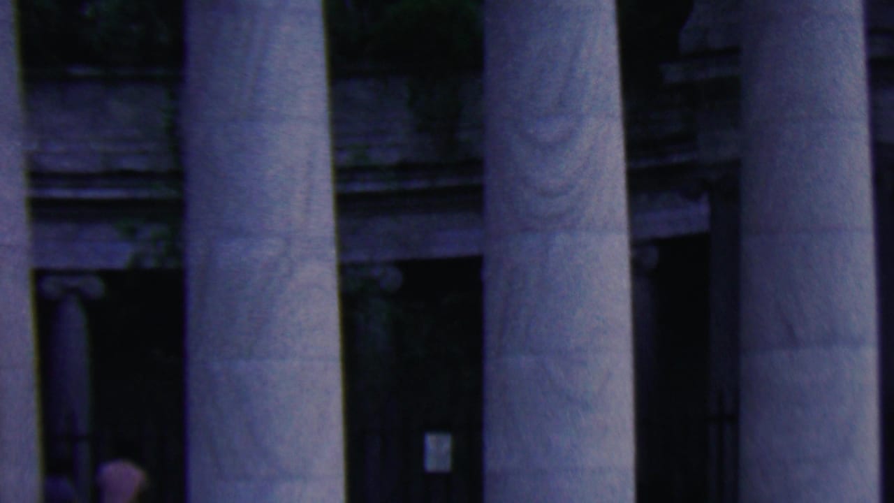 1961 Covington, Kentucky home-movie frame showing tall fluted columns, shadowed entry bays, and a small figure partly visible near the left doorway.